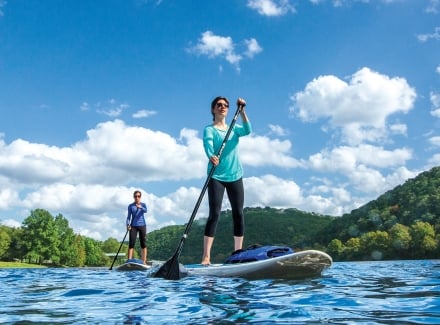 A man and woman use stand-up paddleboards on a sunny day.