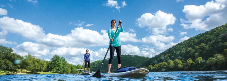A man and woman use stand-up paddleboards on a sunny day.