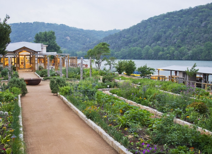 A green garden by the water with several pathways for guests. Green mountains can be seen in the background.
