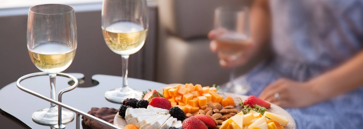 A woman sits at a tray of food consisting of cheeses, almonds, and berries alongside two glasses of wine.