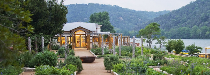 A green garden by the water with several pathways for guests. Green mountains can be seen in the background.