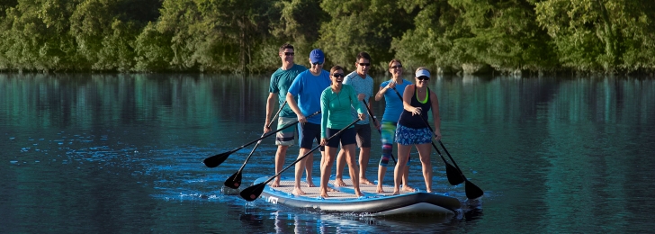 Six friends navigate through the waters of Lake Austin on an oversized paddleboard.