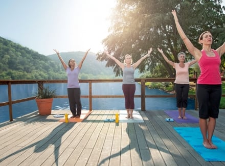 Three women attend a yoga class as their instructor guides them through a series of moves on a deck over the water.