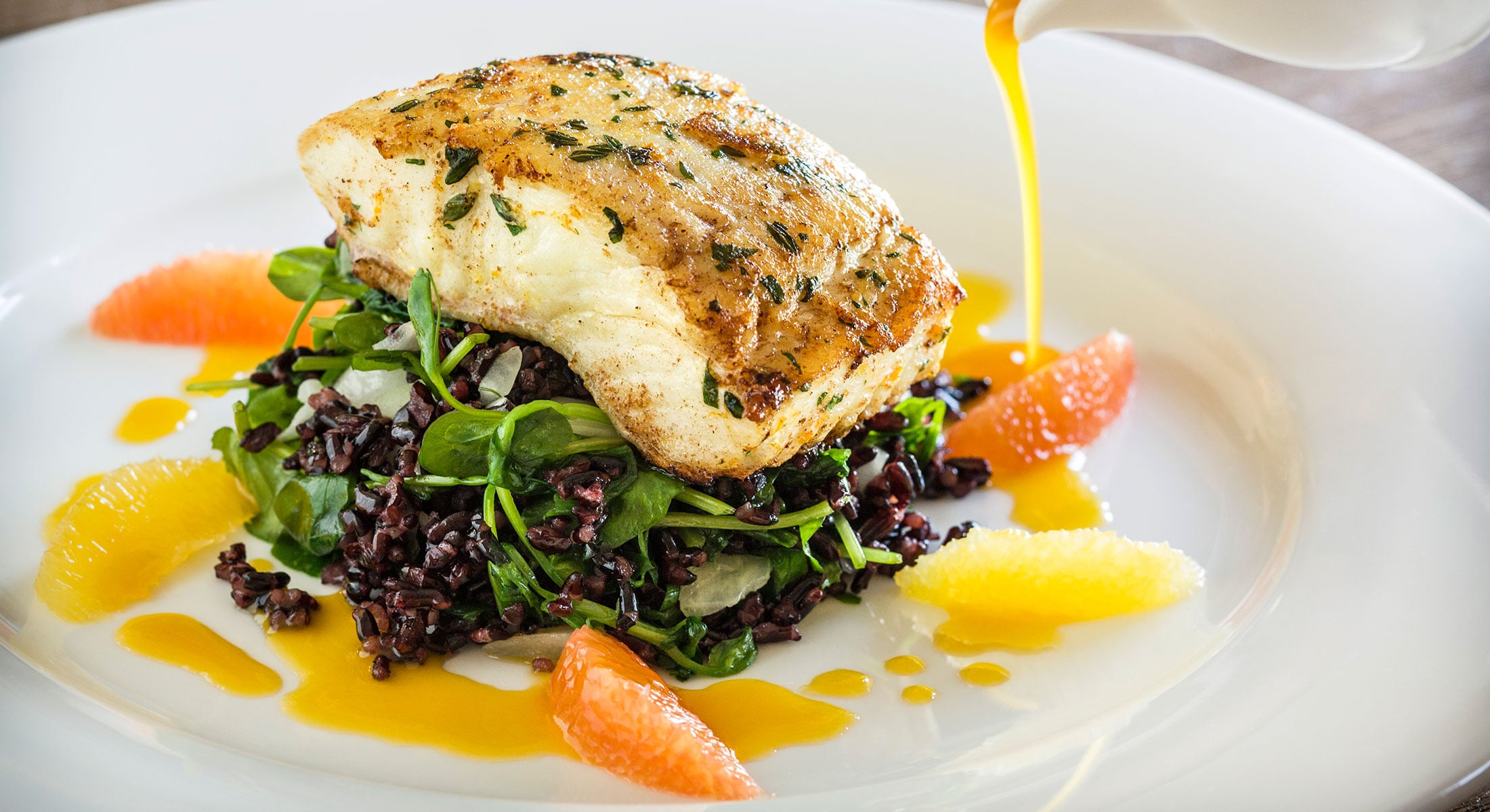 A piece of fish on a bed of greens and rice with citrus and sauce