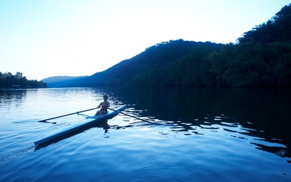 A guest rows in a single scrull rowing boat in the early morning light.