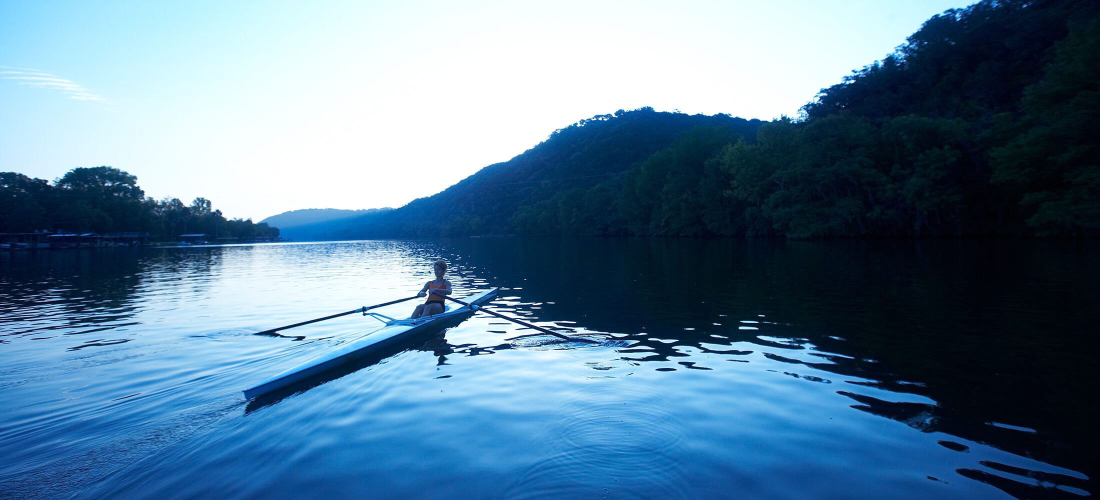 A guest rows in a single scrull rowing boat in the early morning light.