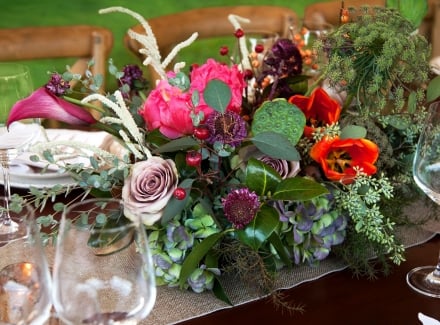An arrangement of colorful flowers surrounded by wine glasses on a dining table.