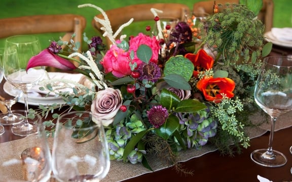 An arrangement of colorful flowers surrounded by wine glasses on a dining table.