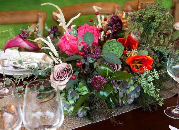 An arrangement of colorful flowers surrounded by wine glasses on a dining table.