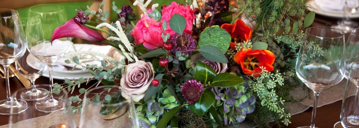 An arrangement of colorful flowers surrounded by wine glasses on a dining table.