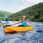 A group of people smiling on the lake enjoying paddling in kayaks, on standup paddleboards, pedal boards, and water sports