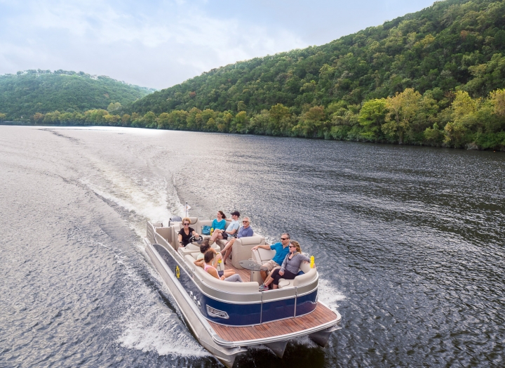 A drone shot of a boat out on the tree-lined lake moving fast through the water. They are relaxed and wearing sunglasses.
