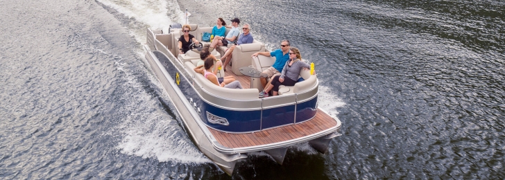 A drone shot of a boat out on the tree-lined lake moving fast through the water. They are relaxed and wearing sunglasses.