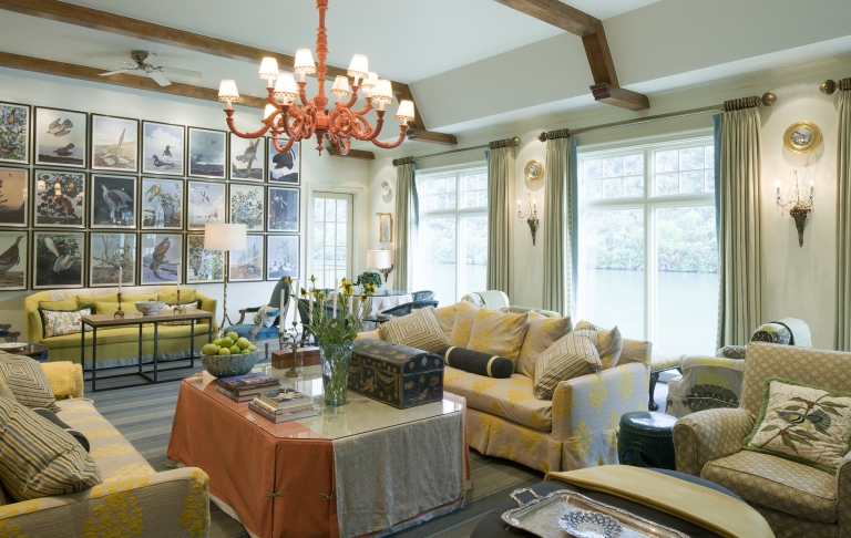 A sage colored room with earthy toned furniture, framed illustrations of birds are on the far wall