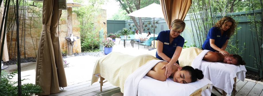 A couple receives a massage outdoors underneath a canopy with gardens in the background.