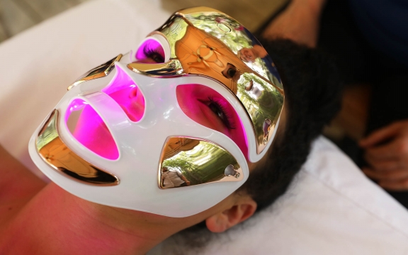 A woman receives a facial enhancement spa treatment wearing a laser therapy mask.