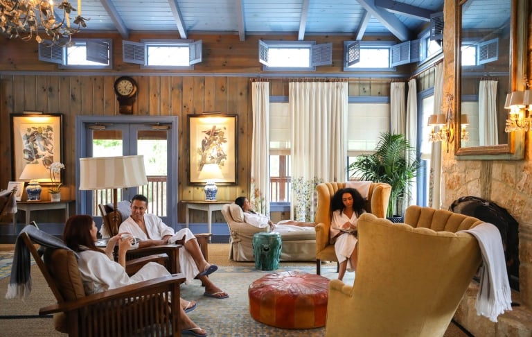 People sitting in the resort lobby in white robes. Natural wood with light blue accents and pastel furniture make the room.