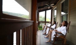 Three women relaxing in bath robes and sitting in chairs on a deck, while looking off into the distance.
