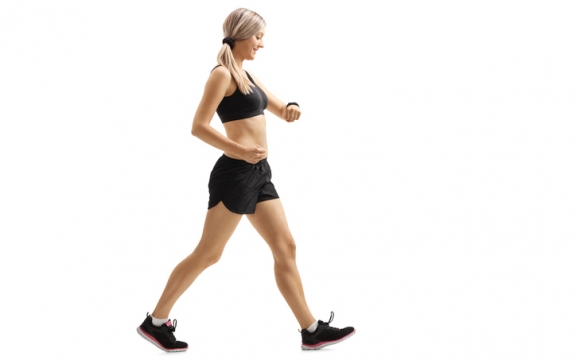 Full length profile shot of a woman walking and checking her sports watch isolated on white background