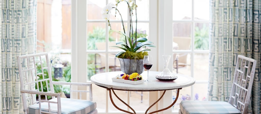 A dining area with a table, chairs, a plant, and a cheese board with wine.
