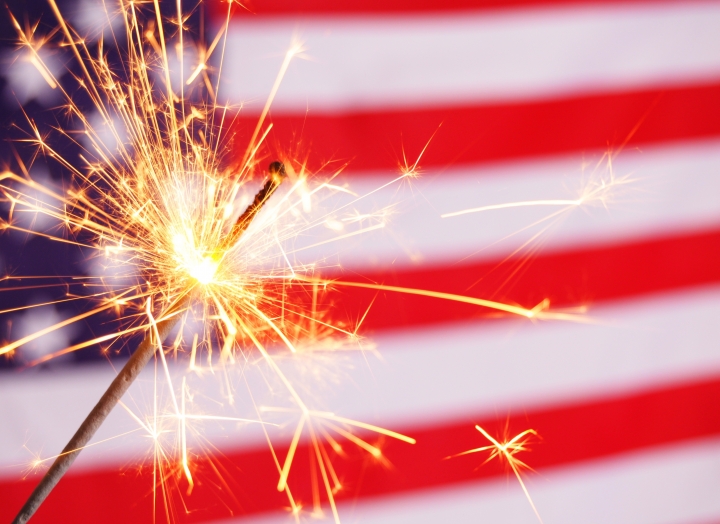 A lit sparkler in front of an American flag.