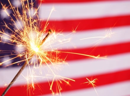 A lit sparkler in front of an American flag.