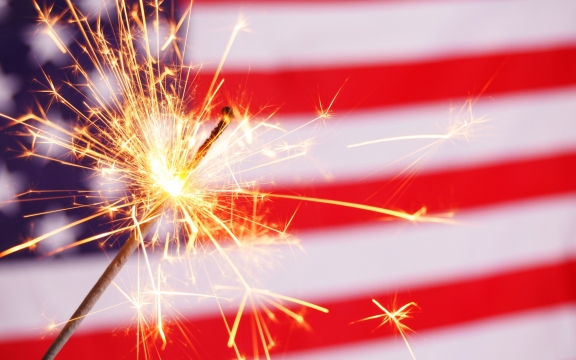 A lit sparkler in front of an American flag.