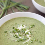 A bowl of green pea soup dressed with pepper and chopped green onion with a swirl of white cream.