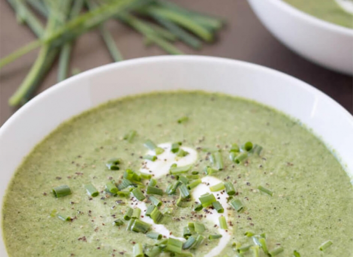 A bowl of green pea soup dressed with pepper and chopped green onion with a swirl of white cream.