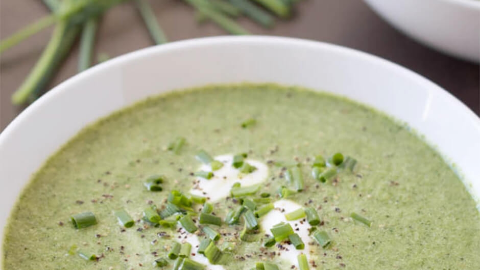 A bowl of green pea soup dressed with pepper and chopped green onion with a swirl of white cream.