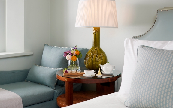 Bedside table with fresh flowers and a lounge chair in the Luxury Garden room