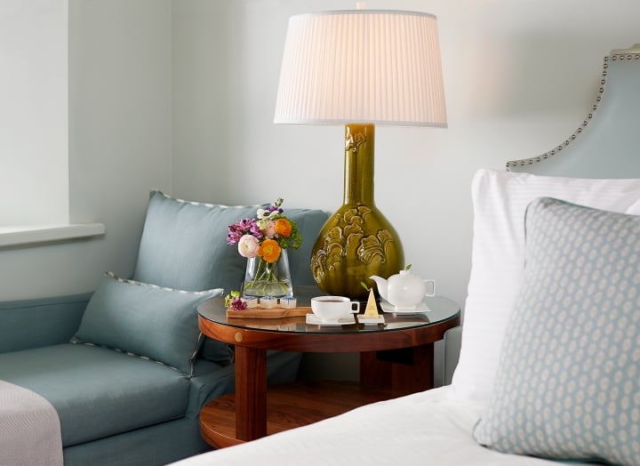 Bedside table with fresh flowers and a lounge chair in the Luxury Garden room
