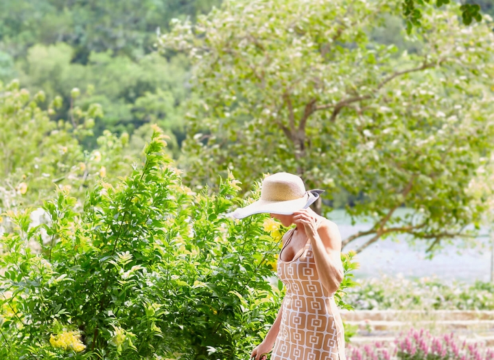 Woman in a long dress and sun hat strolls through the luscious Lake Austin gardens