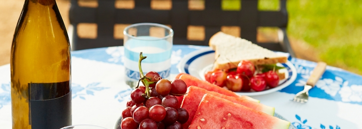 Outdoor table set with wine, sandwiches and fresh fruit