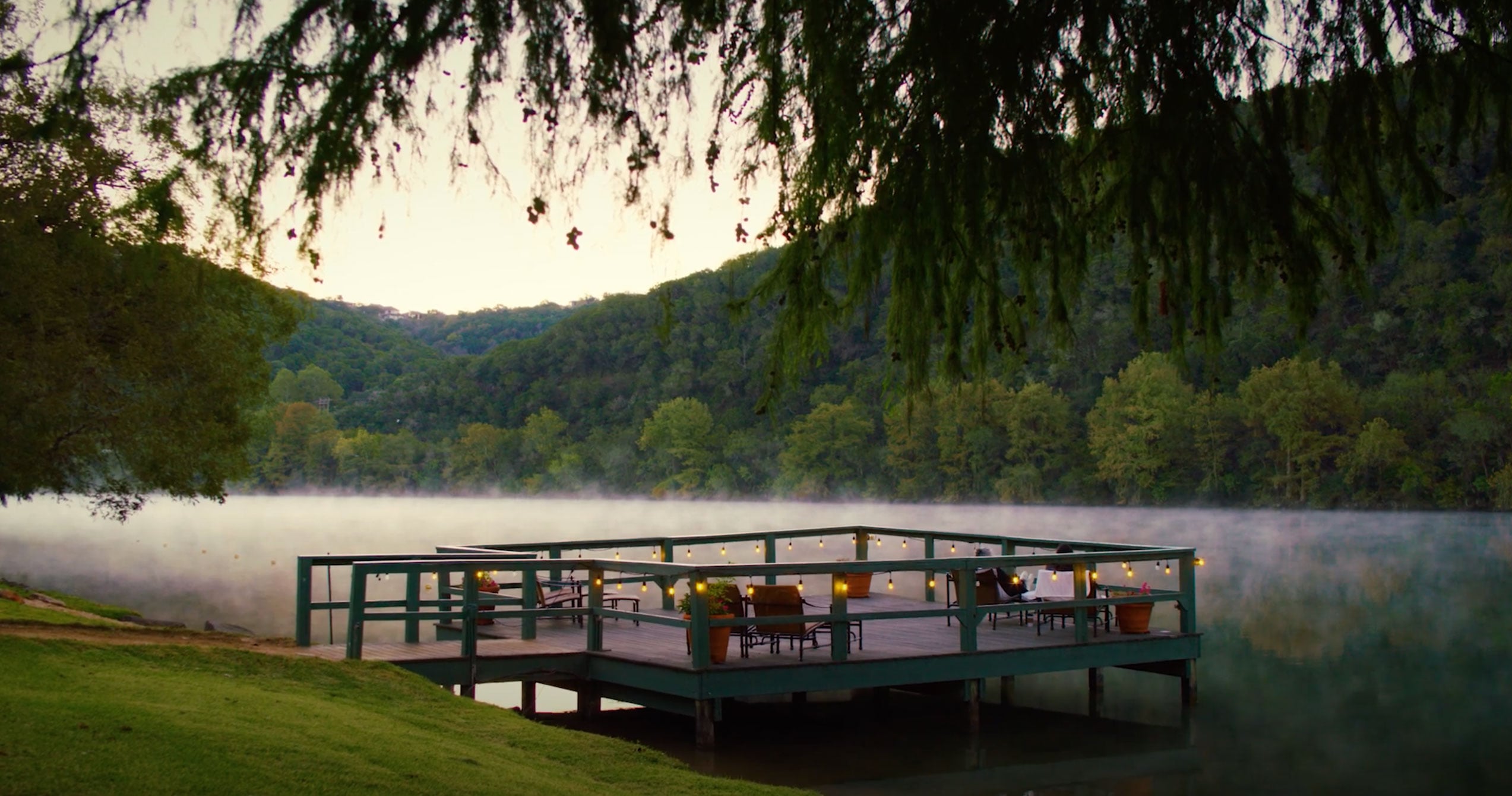A deck overlooking a lake with mountains in the background at dusk or dawn.