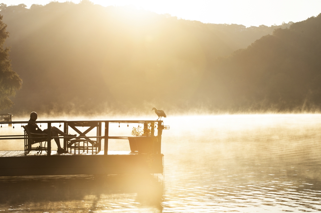 Silhouetted man reading on dock in the early morning with fog coming off the lake at Lake Austin Spa Resort