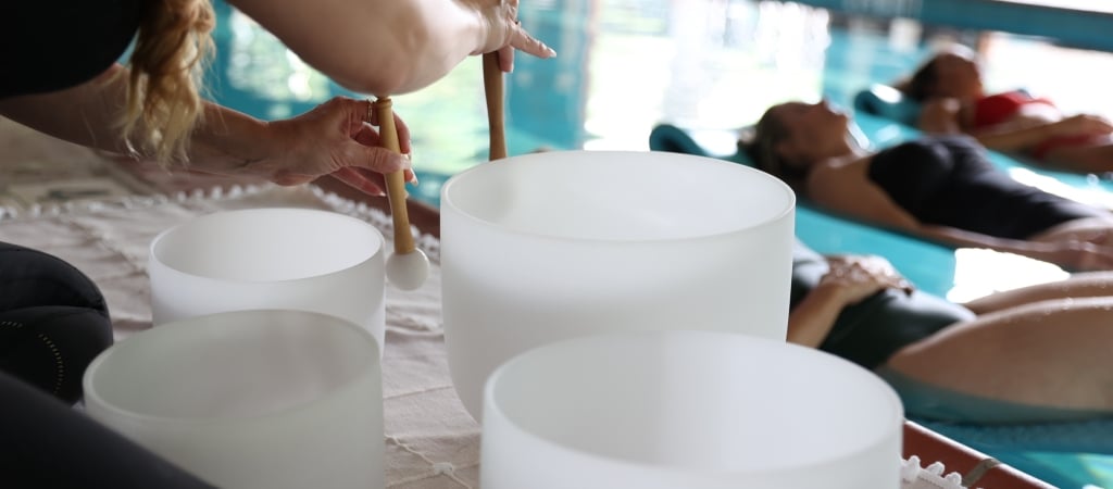 A person playing crystal singing bowls with people lying on mats in the background.