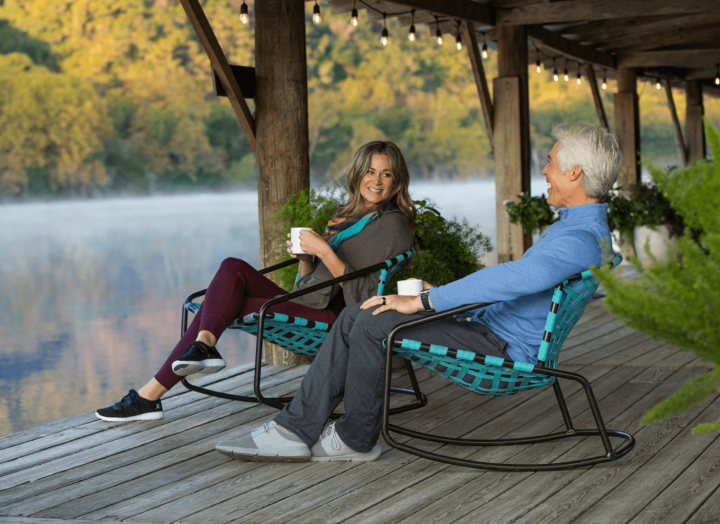 A couple drinking coffee on sitting on outdoor rocking chairs while overlooking the lake
