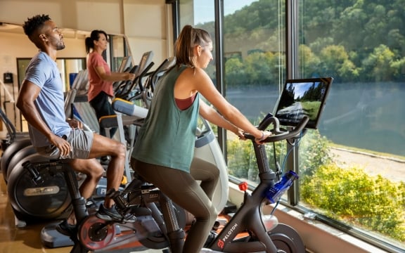 three people working out in the fitness center facing the beautiful lake view