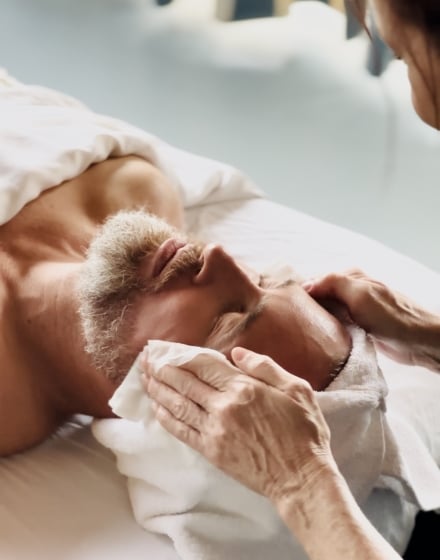 a man lying on a massage table with a towel over his body and a person wiping his face with a towel