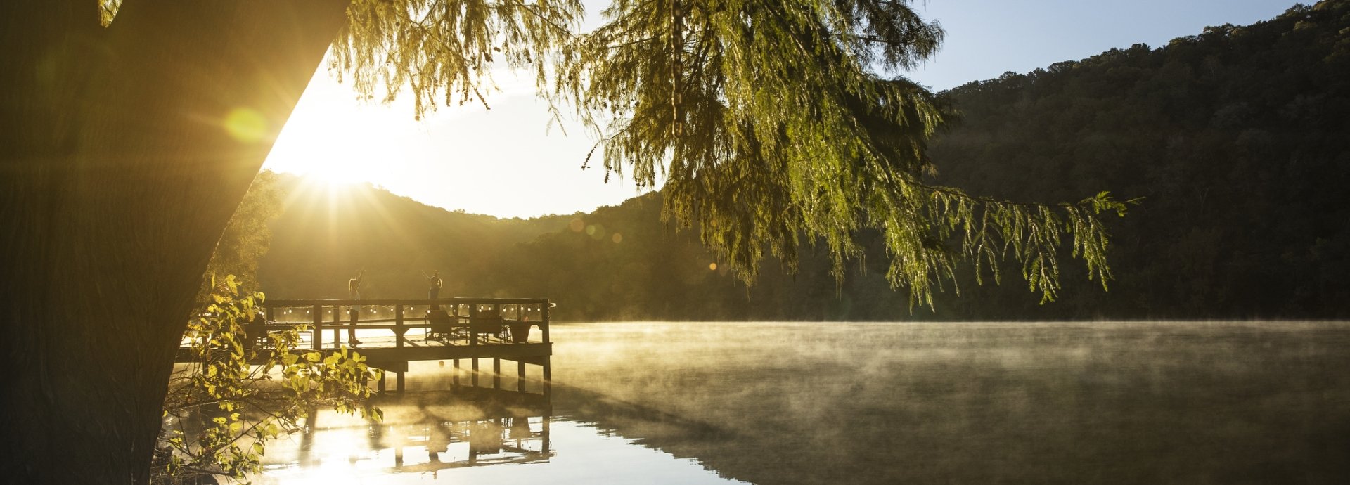 Woman and instructor doing yoga on dock in the early morning with fog coming off the lake at Lake Austin Spa Resort