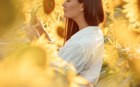 A woman standing in a sunflower field with a flower in her hands