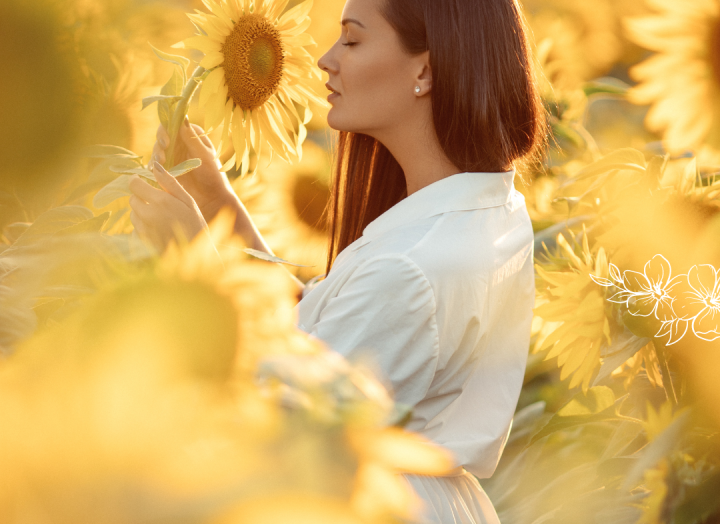A woman standing in a sunflower field with a flower in her hands