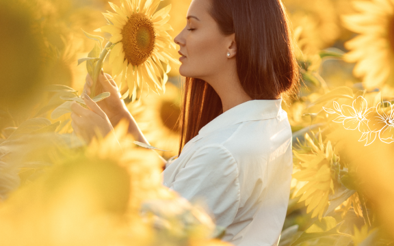 A woman standing in a sunflower field with a flower in her hands
