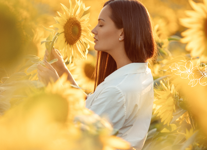 A woman standing in a sunflower field with a flower in her hands