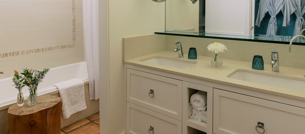 A clean and well-appointed bathroom with a double vanity, mirror, bathtub, and tiled wall.