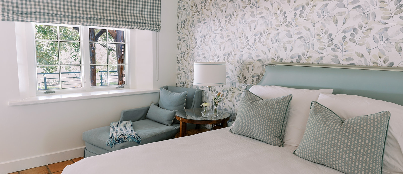 View from inside a room overlooking a lake, featuring a bed, cushion chair, and a beautifully decorated wall with wallpaper