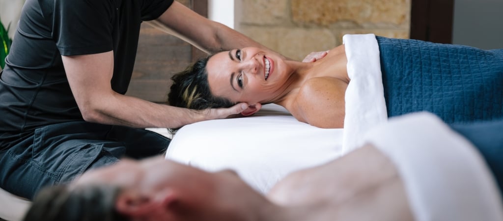 A woman receiving a massage on a table with a stone wall in the background.
