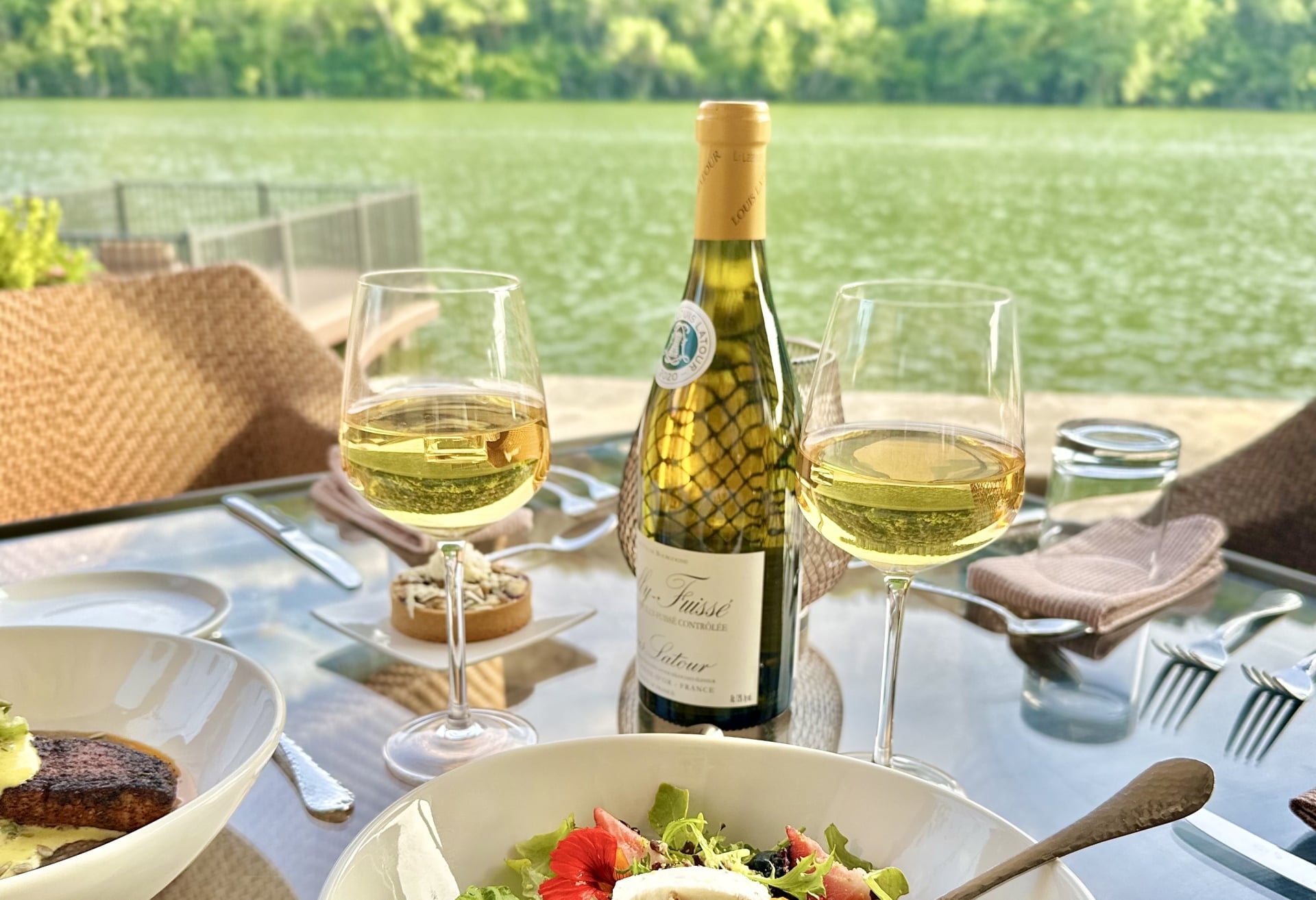 A table set with wine and food overlooking a lake.