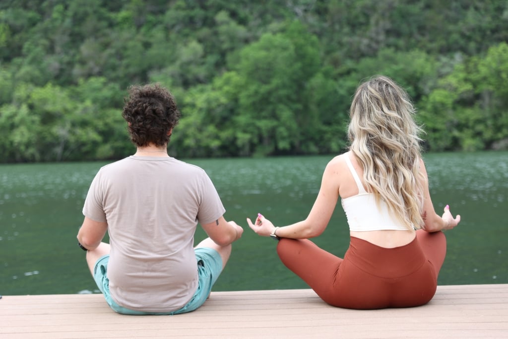 two people sat doing yoga on a boardwalk over a lake